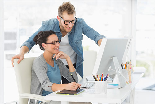 smiling man and woman look at computer